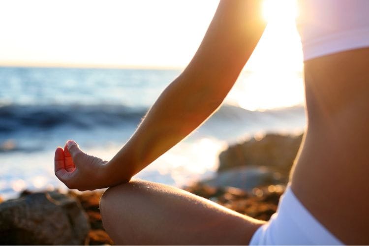 Woman on the beach meditating for self-care, following mental health tips.